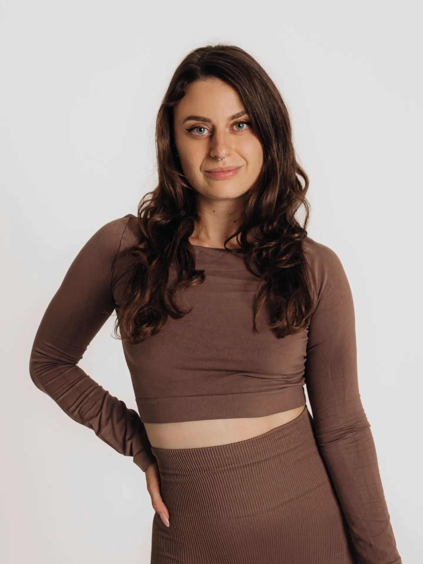 Randa Romanova smiling in a fitted brown practice set against a white studio background